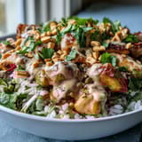 A close-up of creamy peanut sauce drizzled over succulent chicken and fresh veggies in a colorful Thai-inspired meal prep bowl.  