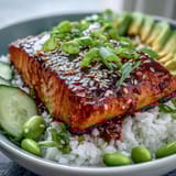 Spicy and sweet salmon bowl with drizzled sriracha mayo, sesame seeds, and vibrant green onions for garnish.