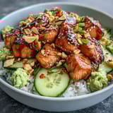 Fusion-style avocado salmon bowl topped with crunchy peanuts, fresh cucumber, and a dab of wasabi on a warm rice base.
