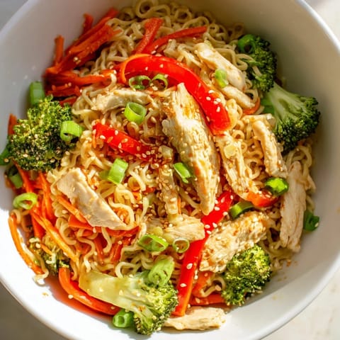 A close-up of Spicy Ramen Stir-Fry with glistening noodles, julienned carrots, and a sprinkle of toasted sesame seeds.