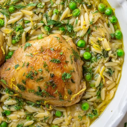 Golden brown chicken pieces nestle in a one-pan skillet with tender orzo, bright green peas, and flecks of fresh dill and parsley, all glistening in a zesty lemon sauce ready to be served.