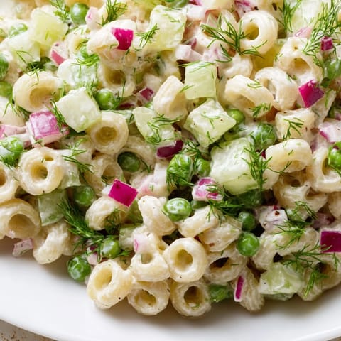 A close-up of creamy dill pickle pasta salad with ditalini, peas, and crunchy pickles, ready to be enjoyed at a backyard barbecue.
