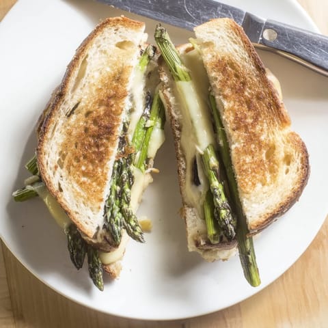 Golden sourdough slices hold melted Brie and charred asparagus spears for a savory Asparagus & Brie Grilled Cheese, served warm and ready to enjoy.  