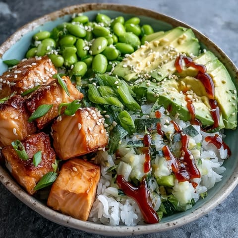Flaky baked salmon cubes glisten atop fluffy jasmine rice in this vibrant salmon rice bowl, with edamame and creamy avocado slices.