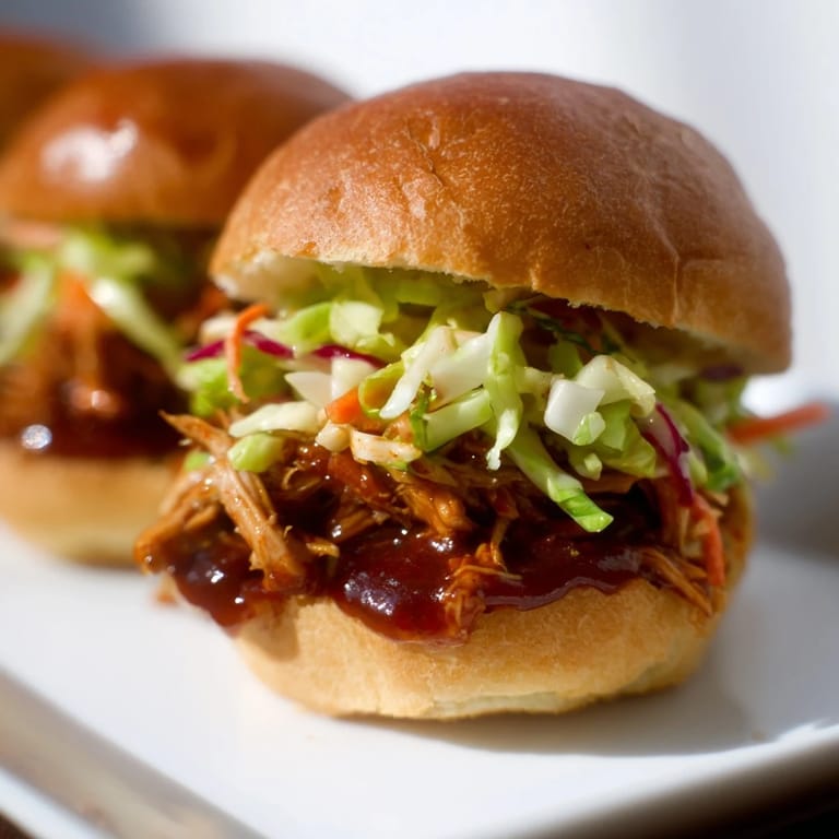 Two BBQ Chicken Sliders on a wooden board with melted butter toasted buns and tangy coleslaw.  