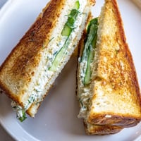Golden-brown Whipped Feta Spring Grilled Cheese slices on a wooden board, revealing a creamy, vibrant green filling speckled with fresh dill and lemon zest.
