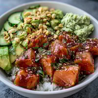 Brightly colored avocado salmon bowl with marinated fish, creamy avocado slices, and a drizzle of chili oil over sushi rice.